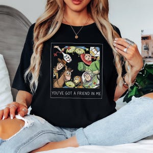 Pode incluir: Camiseta preta com um gr&aacute;fico colorido de personagens do filme de anima&ccedil;&atilde;o "Toy Story". O gr&aacute;fico &eacute; emoldurado em um ret&acirc;ngulo branco e inclui o texto "YOU'VE GOT A FRIEND IN ME."