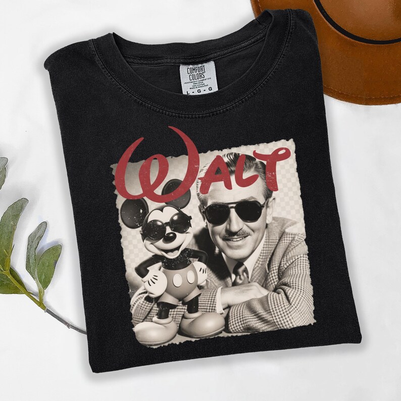 Puede incluir: Camiseta negra con una imagen en tonos sepia de Walt Disney y Mickey Mouse con gafas de sol. La palabra "Walt" est&aacute; impresa en rojo encima de la imagen. La camiseta est&aacute; doblada.