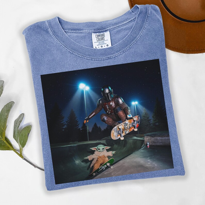 May include: Blue Comfort Colors t-shirt featuring a graphic of The Mandalorian and Grogu skateboarding in a skate park at night. The image includes the Comfort Colors logo.