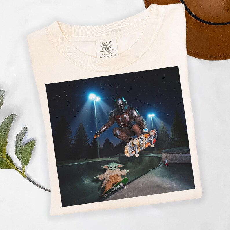 May include: Cream-colored t-shirt featuring a graphic of The Mandalorian and Grogu skateboarding in a skate park at night. The image is centered on the shirt, with the Comfort Colors logo visible at the top.