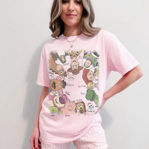 Colorful retro cartoon characters with names like Woody and Buzz in a playful layout on a t-shirt.