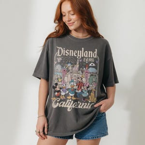 May include: Charcoal grey t-shirt with a Disneyland graphic featuring Mickey Mouse, Donald Duck, and friends. The shirt displays the text "Disneyland Est 1955 California" in a vintage design.