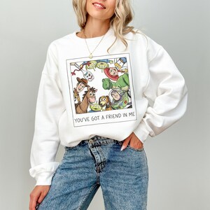 Pode incluir: Camisola branca com um gr&aacute;fico emoldurado de personagens animados. O gr&aacute;fico inclui um cavalo, um c&atilde;o e outros personagens. O texto "YOU'VE GOT A FRIEND IN ME" est&aacute; impresso abaixo. A camisola &eacute; feita de um material macio.