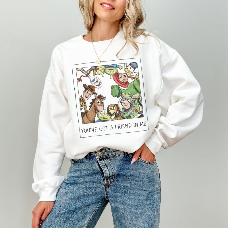 Pode incluir: Camisola branca com um gr&aacute;fico emoldurado de personagens animados. O gr&aacute;fico inclui um cavalo, um c&atilde;o e outros personagens. O texto "YOU'VE GOT A FRIEND IN ME" est&aacute; impresso abaixo. A camisola &eacute; feita de um material macio.