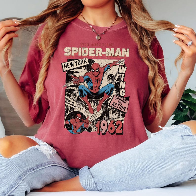 May include: Maroon t-shirt featuring a vintage Spider-Man graphic. The design includes the text "The Amazing Spider-Man," "New York," and "1962." The graphic shows Spider-Man in action, with a comic book style.