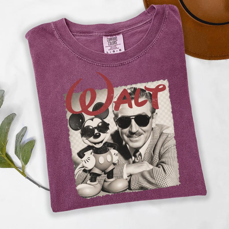 Puede incluir: Una camiseta Comfort Colors color granate con un gr&aacute;fico de Mickey Mouse y Walt Disney. El gr&aacute;fico es en blanco y negro con la palabra "Walt" en rojo. La camiseta est&aacute; doblada.