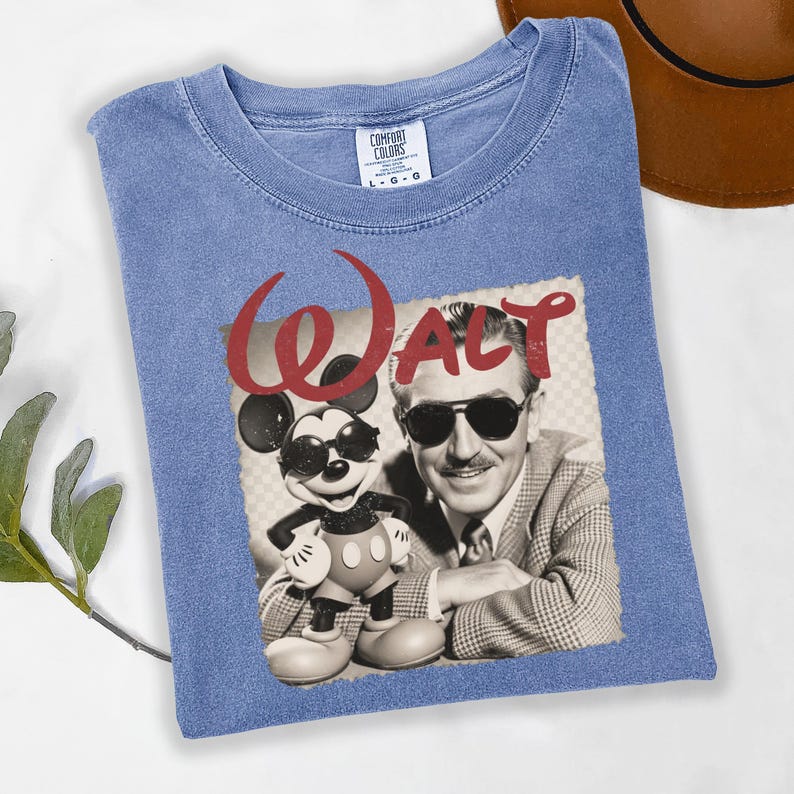 Puede incluir: Camiseta azul con un gr&aacute;fico de Walt Disney y Mickey Mouse con gafas de sol. La palabra "WALT" est&aacute; impresa en rojo encima de la imagen. La camiseta es de un material suave.