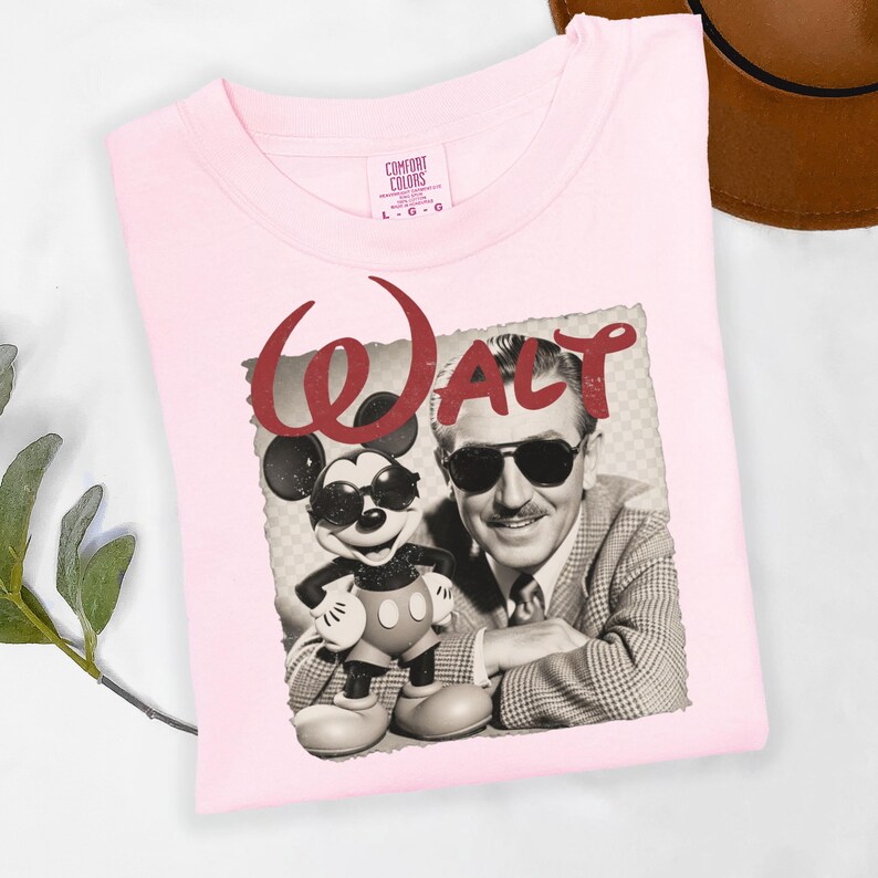 Puede incluir: Camiseta rosa claro con una imagen en blanco y negro de Mickey Mouse y Walt Disney. La palabra "WALT" est&aacute; impresa en rojo encima de la imagen. La camiseta es de la marca Comfort Colors, talla L-G.
