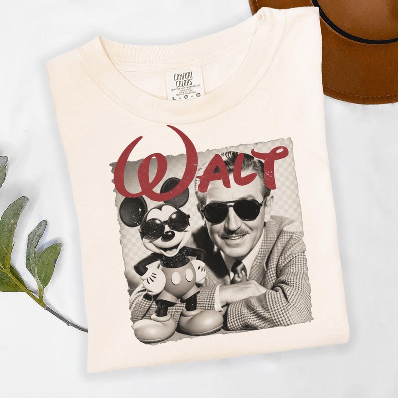 Puede incluir: Camiseta color crema con un gr&aacute;fico de estilo vintage de Mickey Mouse con gafas de sol junto a un retrato de Walt Disney. La palabra "WALT" est&aacute; impresa en rojo encima de la imagen. La camiseta es de la marca Comfort Colors, talla L-G.
