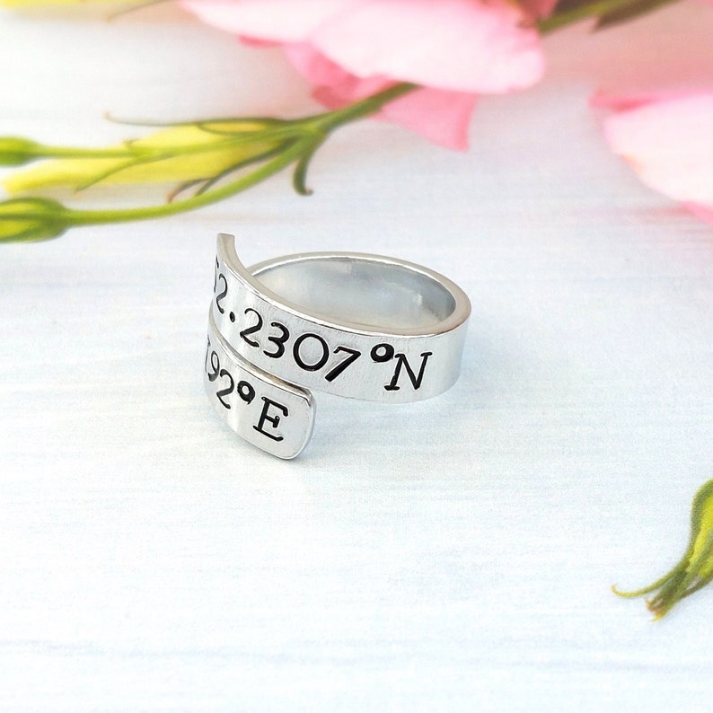 A statement aluminium adjustable wrap ring with the example coordinates "52.230 0.1192°E" hand-stamped on it.