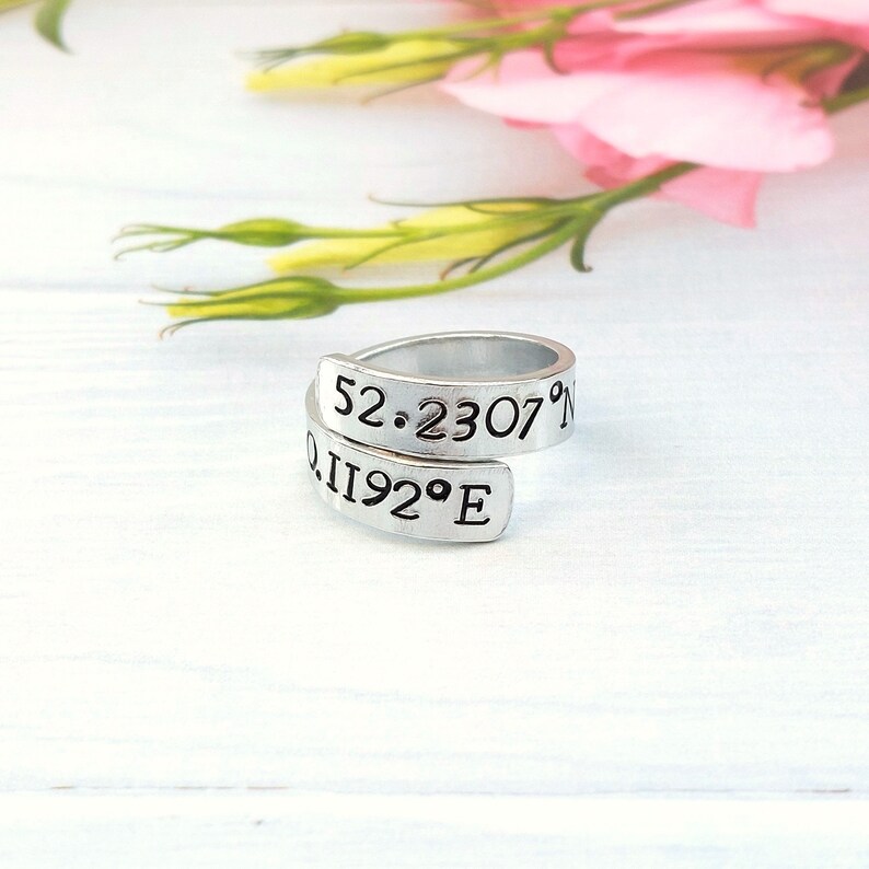 A statement aluminium adjustable wrap ring with the example coordinates "52.230 0.1192°E" hand-stamped on it.