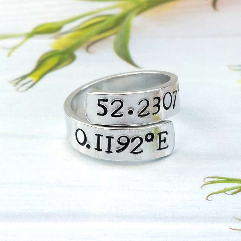 A statement aluminium adjustable wrap ring with the example coordinates "52.230 0.1192°E" hand-stamped on it.