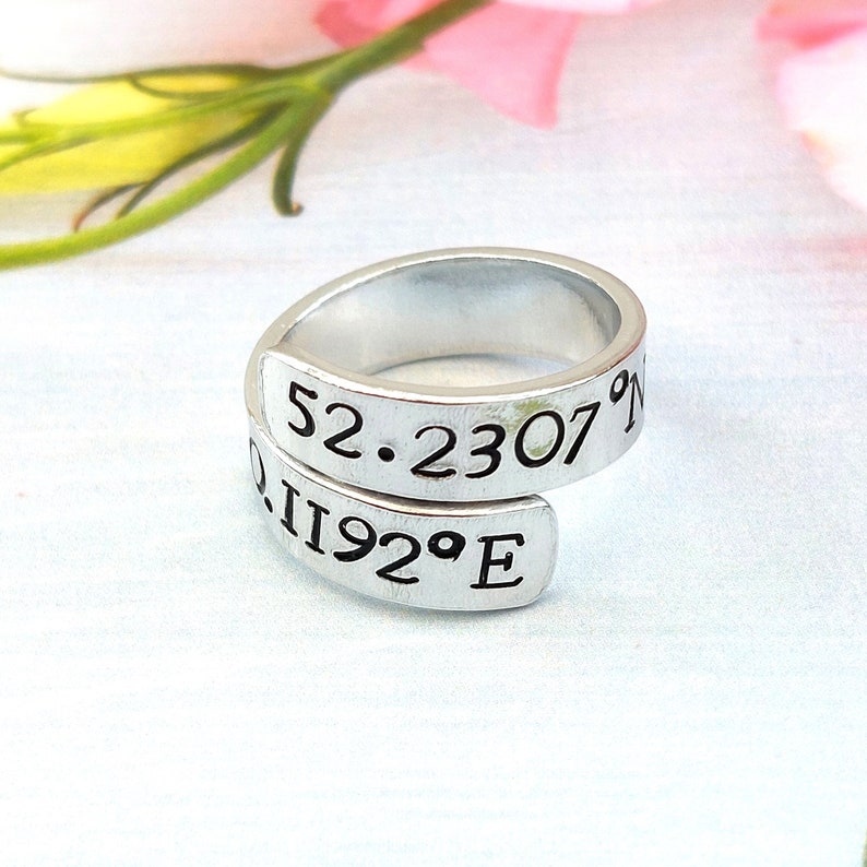 A statement aluminium adjustable wrap ring with the example coordinates "52.230 0.1192°E" hand-stamped on it.