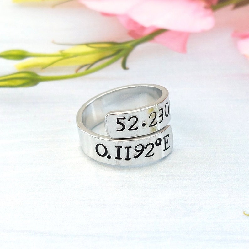 A statement aluminium adjustable wrap ring with the example coordinates "52.230 0.1192°E" hand-stamped on it.