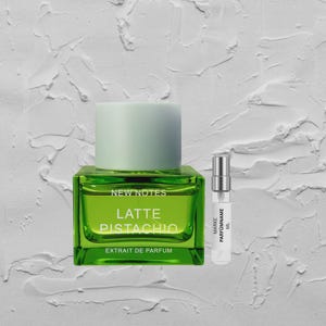 Könnte beinhalten: Eine grüne Parfümflasche mit hellgrünem Deckel, beschriftet mit "Latte Pistachio" und "Extrait de Parfum". Neben der Flasche befindet sich ein kleines Probenfläschchen. Der Hintergrund ist eine strukturierte weiße Oberfläche.