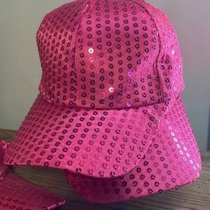 May include: A pink sequined baseball cap with a curved brim. The cap is made of a soft, shiny fabric and is covered in small, round sequins.