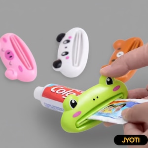 May include: A collection of colorful, animal-shaped toothpaste tube squeezers. The squeezers include a pink pig, a white panda, an orange bear, and a green frog. A tube of toothpaste is being squeezed by the frog-shaped squeezer.