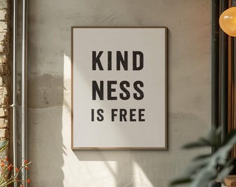 May include: A framed wall art print with the words "KINDNESS IS FREE" in bold black letters on a cream-colored background. The frame is a light brown color, and the art is hanging on a textured gray wall.