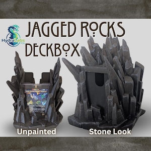 Könnte beinhalten: Zwei zackenförmige Deckboxen, eine unbemalt und eine im Stein-Look. Die Boxen sind für Sammelkarten konzipiert. Der Text "JAGGED ROCKS DECKBOX" ist über den Boxen zu sehen, mit dem Hydra Labs TCG-Logo links.