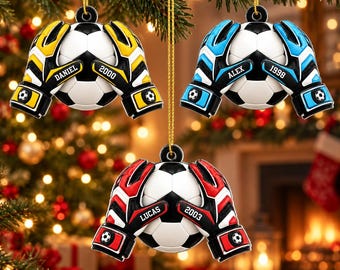 Puede incluir: Tres adornos colgantes con forma de balones de fútbol sostenidos por guantes de portero. Uno es amarillo y negro con DANIEL 2000, otro azul y negro con ALEX 1998, y otro rojo y negro con el texto LUCAS 2003.