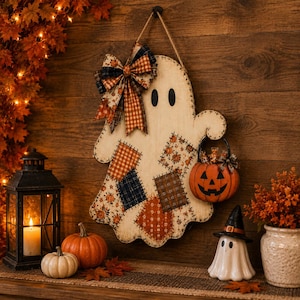May include: A wooden ghost wall hanging featuring a distressed cream finish, black oval eyes, and a decorative bow made of plaid and floral fabric. The ghost is adorned with fabric patches in orange, brown, and navy, and holds a small orange jack-o'-lantern.