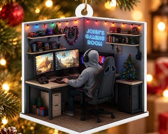 Puede incluir: Un adorno navideño cuadrado que muestra una escena de sala de juegos en miniatura con una persona con sudadera gris sentada en una silla de juego negra frente a dos monitores. La pared muestra el texto azul neón John's Gaming Room.