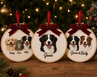 Puede incluir: Tres bastidores de bordado circulares de madera con retratos de mascotas personalizados sobre tela crema. Cada bastidor tiene un lazo de terciopelo rojo oscuro. Los retratos muestran perros y un gato con nombres bordados debajo.