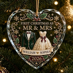 May include: A heart-shaped glass Christmas ornament featuring the text FIRST CHRISTMAS AS MR & MRS, WILLIAM & SOPHIA, and 2026. The design includes a dark green suit, a white wedding dress, holly leaves, red berries, and gold scrollwork.