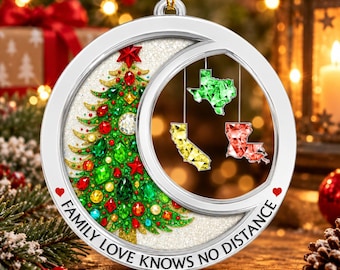Puede incluir: Un adorno navideño circular de tono plateado con fondo brillante, un árbol decorado con gemas rojas y verdes, y tres dijes colgantes con forma de estados en verde, amarillo y rojo. El texto dice FAMILY LOVE KNOWS NO DISTANCE.