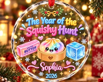 Puede incluir: Un adorno circular de acrílico transparente con el texto The Year of the Squishy Hunt, una bola de masa arcoíris en una vaporera de madera, una barra de mantequilla rosa, un cubo de hielo azul, el nombre Sophia y el año 2026.