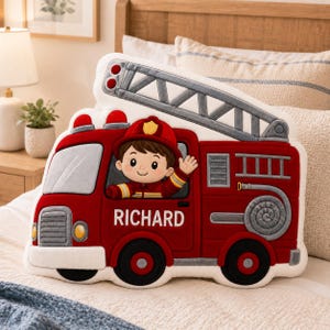 May include: A plush, red fire truck-shaped pillow with a smiling firefighter waving from the driver's seat. The pillow features the name "RICHARD" and a gray ladder. The design includes red lights and a gray hose.