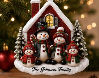 Puede incluir: Un adorno navideño con forma de casa que muestra cuatro muñecos de nieve etiquetados como Dad, Mom, Emma y Jack. La casa roja tiene un techo brillante y una chimenea. La base es blanca y nevada con el texto The Johnson Family en letra negra.