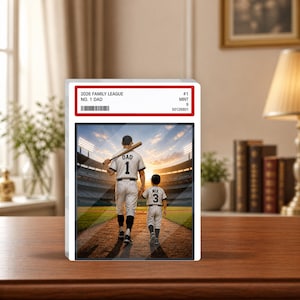 May include: A framed baseball card featuring a father and child walking on a baseball field at sunset. The card reads "2026 Family League No. 1 Dad" and includes the number "1" on the father's jersey and "3" on the child's.