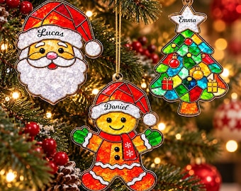 Puede incluir: Tres adornos navideños colgantes con diseño de vidriera: un Santa Claus con el nombre Lucas, un hombre de jengibre con el nombre Daniel y un árbol de Navidad con una estrella que lleva el nombre Emma.