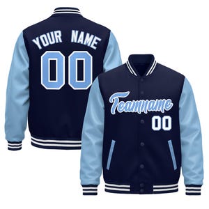 May include: Navy blue and light blue varsity jacket with white accents. The jacket features light blue sleeves, a navy body, and the text "Your Name" and the number "00" on the back. The front of the jacket has the text "Teamname" and the number "00".