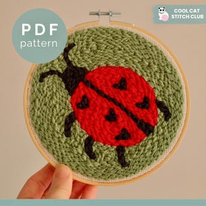 May include: A hand-stitched embroidery hoop featuring a red ladybug with black spots on a green background. The text "PDF pattern" is in a light blue circle. The text "COOL CAT STITCH CLUB" is in the upper right corner.