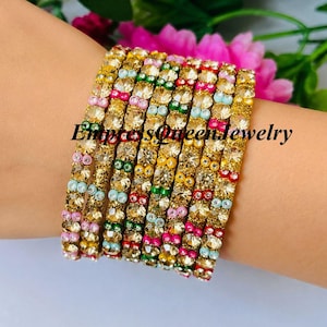 May include: A set of seven stacked bangles featuring clear faceted stones and small colorful accent beads in pink, green, blue, and yellow. The bangles have a metallic gold-tone finish and are marked with the text EmpressQueenJewelry.