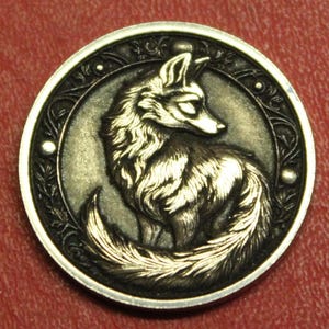 May include: A silver-toned round pendant featuring a detailed relief of a fox. The fox is depicted with intricate fur and is surrounded by an ornate border. The pendant has a vintage or antique aesthetic.