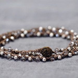 May include: A multi-strand bracelet with silver beads and a brown cord, featuring a decorative metal button.