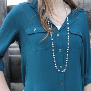 May include: A teal blue button-down shirt with a long pearl necklace.