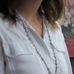 May include: A silver chain necklace with light green gemstone beads. The necklace is worn by a person with long brown hair.
