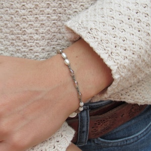 May include: A brown and white beaded bracelet with a braided cord. The bracelet is worn on a person's wrist.