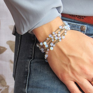 May include: A multi-strand bracelet with light blue beads and brown cord. The bracelet is worn on a person's wrist.