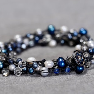 May include: A multi-strand bracelet with blue and white beads, including pearls, and a black cord. The bracelet has a decorative button closure.