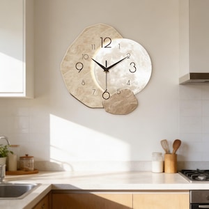 Könnte beinhalten: Eine moderne Wanduhr mit einem einzigartigen Design. Die Uhr hat ein kreisförmiges Zifferblatt mit mondähnlicher Textur, umgeben von unregelmäßigen, steinartigen Formen. Die Zeiger sind schwarz, und die Zahlen sind in einer einfachen, gut lesbaren Schriftart gehalten. Die Uhr ist an einer weißen Wand befestigt.