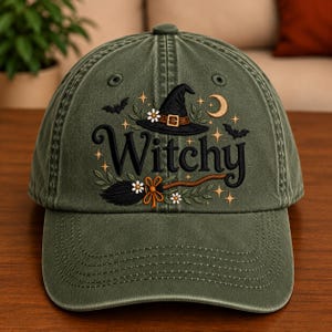 May include: An olive green baseball cap featuring embroidered designs including a black witch hat, a broomstick, bats, a crescent moon, small white flowers, and gold stars. The word "Witchy" is embroidered in large black script across the centre.
