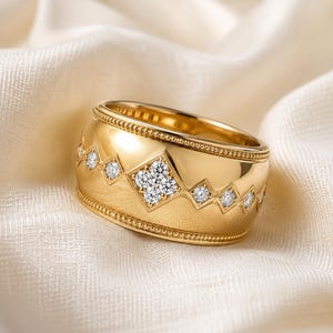 Peut inclure: Une large bague en or avec un groupe de diamants central serti dans un cadre en forme de losange, flanqué de diamants individuels plus petits dans des sertis en losange. Les bords de la bague présentent une texture perlée délicate.