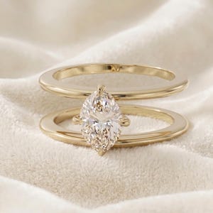 Op de afbeelding: Een gouden ring met dubbele band en een centrale edelsteen in marquise-slijpvorm. De twee gladde, gepolijste gouden banden zijn verbonden door de in klauwen gezette marquise-steen, die horizontaal tussen de parallelle banden is geplaatst.
