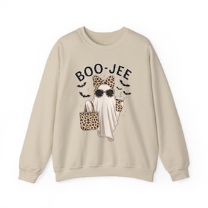 May include: A beige crewneck sweatshirt featuring a graphic of a ghost wearing leopard print sunglasses and a matching bow. The ghost holds a leopard print tote bag and a drink cup, surrounded by black bats and the text BOO-JEE in black letters.
