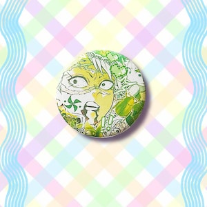 Puede incluir: Un bot&oacute;n redondo con una ilustraci&oacute;n de dibujos animados que presenta una cara sorprendida con tonos verdes y amarillos. El bot&oacute;n tiene un fondo blanco con detalles verdes y amarillos. El fondo es un patr&oacute;n de cuadros pastel.